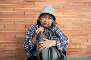 Arm müde betont deprimiert Alten asiatisch Frau obdachlos Sitzung auf das Straße im das Schatten von das Gebäude und betteln zum Hilfe und Geld, Alten asiatisch Frau verlassen Konzept foto