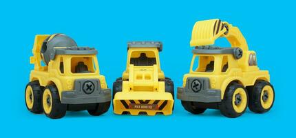 Gelb Plastik Spielzeug von Beton Rührgerät und Bagger LKW isoliert auf Blau Hintergrund. schwer Konstruktion Fahrzeug auf niedrig Winkel schießen. foto