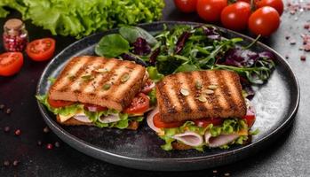leckeres Sandwich mit knusprigem Toast, Schinken, Salat und Tomaten foto