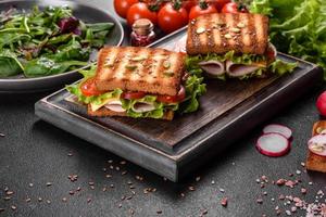 leckeres Sandwich mit knusprigem Toast, Schinken, Salat und Tomaten foto