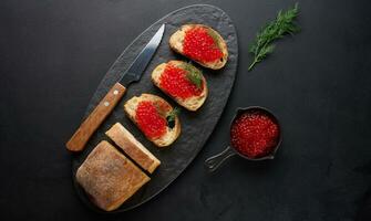 rot Kaviar auf Scheiben von Weiß Weizen Brot auf ein schwarz Tisch, Konzept von Luxus und Gourmet Küche foto