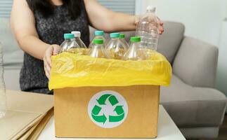 Zuhause recyceln Öko Grün Null Konzept Frau werfen leeren Plastik Flasche im Recycling Behälter mit Gelb Müll Taschen beim heim. foto