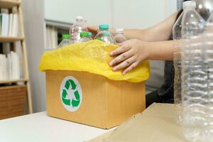 Zuhause recyceln Öko Grün Null Konzept Frau werfen leeren Plastik Flasche im Recycling Behälter mit Gelb Müll Taschen beim heim. foto