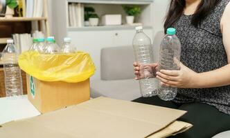 Zuhause recyceln Öko Grün Null Konzept Frau werfen leeren Plastik Flasche im Recycling Behälter mit Gelb Müll Taschen beim heim. foto