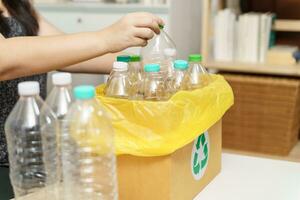 Zuhause recyceln Öko Grün Null Konzept Frau werfen leeren Plastik Flasche im Recycling Behälter mit Gelb Müll Taschen beim heim. foto