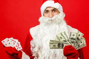 Santa claus Hände halten Geld und spielen Karten auf rot Hintergrund foto