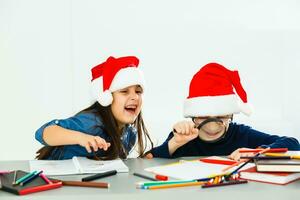 Schreiben Brief zu Weihnachtsmann. Kinder im Santa Hüte machen Wunsch aufführen von die Geschenke zum Weihnachten. Winter Feiertage. Junge und Mädchen, Bruder und Schwester zeichnen foto