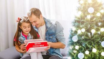 Vater gibt Tochter ein Weihnachten Geschenk im das Wohnzimmer foto