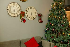 Weihnachten Winter Urlaub Konzept. dekoriert Weihnachten Baum, gemütlich Sofa mit rot Kopfkissen, Uhren auf ein Mauer foto