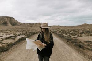 Frau mit Karte Stehen auf Schmutz Straße im unfruchtbar Landschaft foto