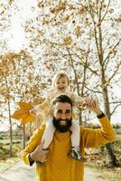 Vater Tragen seine wenig Tochter auf Schultern im das Morgen im ein Park im Herbst foto