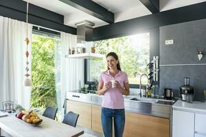 Lachen Frau beim Zuhause im Küche mit Tasse von Kaffee foto