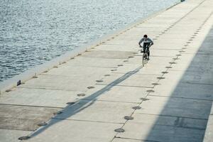 jung Mann Reiten Fahrrad auf direkt am Wasser Promenade beim das Flussufer foto