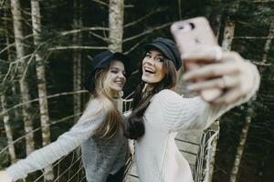 zwei glücklich jung Frauen auf ein Suspension Brücke nehmen ein Selfie foto