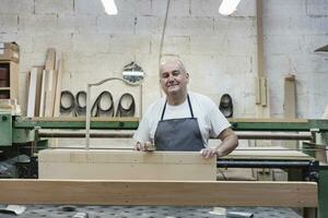 lächelnd reifen Mann halten Planke während Stehen beim Werkstatt foto