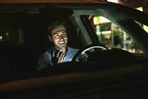 glücklich jung Mann mit Zelle Telefon im Auto beim Nacht foto