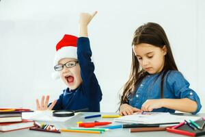 Schreiben Brief zu Weihnachtsmann. Kinder im Santa Hüte machen Wunsch aufführen von die Geschenke zum Weihnachten. Winter Feiertage. Junge und Mädchen, Bruder und Schwester zeichnen foto