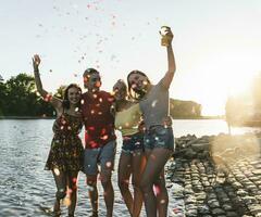 Konfetti um Gruppe von glücklich freunde haben Spaß im ein Fluss beim Sonnenuntergang foto