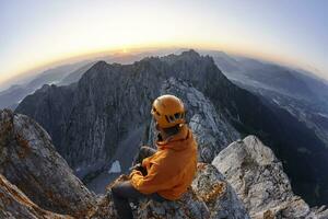 Bergsteiger mit Orange Helm Sitzung auf ellmauer Halt beim Sonnenaufgang, wilder Kaiser, ellmauer Halt, Tirol, Österreich foto