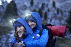 zwei glücklich jung Frauen tragen Scheinwerfer Umarmen im das Berge foto