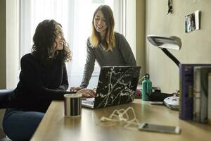 zwei jung Frauen Teilen Laptop beim Zuhause foto