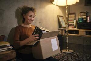 lächelnd jung Frau Auspacken Paket beim Zuhause foto