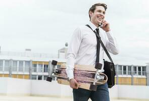 glücklich Geschäftsmann mit Zelle Telefon und Skateboard Gehen beim Parkplatz Garage foto