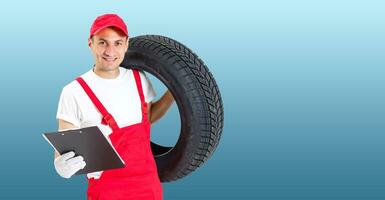 Auto Mechaniker Tragen Reifen auf Blau Hintergrund. glücklich Mann lächelnd amd suchen in Kamera foto