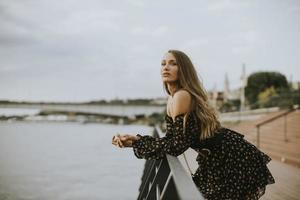 junge brünette Frau mit langen Haaren, die am Flussufer steht foto