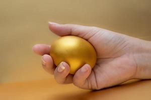 Frauenhand, die goldenes Ei am goldenen Hintergrund hält foto