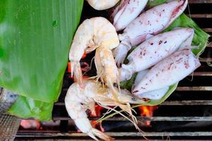 frische Meeresfrüchte wie Garnelen, Tintenfisch und Fisch werden traditionell mit eingewickelten Bananenblättern über einem rauchigen Holzkohlegrill gebraten. Es ist ein köstliches Abendessen für Grillpartys, Picknicks oder Essen im Restaurant. foto