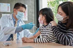 männlicher Arzt impfen asiatisches Mädchen in der Kinderklinik. foto