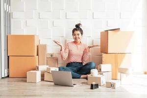asiatische Geschäftsinhaberin, die zu Hause mit Verpackungsbox am Arbeitsplatz arbeitet - Online-Shopping-KMU-Unternehmer oder freiberufliches Arbeitskonzept