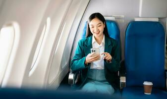 attraktiv asiatisch weiblich Passagier von Flugzeug Sitzung im komfortabel Sitz während Arbeiten Laptop und Tablette mit spotten oben Bereich mit kabellos Verbindung. Reise im Stil, Arbeit mit Anmut. foto