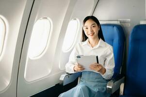 Porträt von erfolgreich asiatisch Geschäftsfrau oder Unternehmer im ein formal passen auf ein Flugzeug Sitzung im Geschäft Klasse mit ein Telefon, Computer Laptop. Reise im Stil, Arbeit mit Anmut. foto