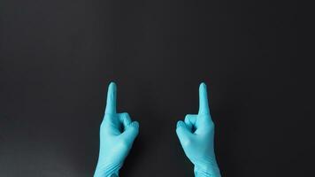 zwei Hand ist tragen Blau Arzt Handschuhe und Punkt das Finger auf schwarz Hintergrund. foto