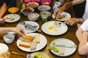 Mann Essen gebraten Eier Frühstück mit freunde auf hölzern Tisch. foto