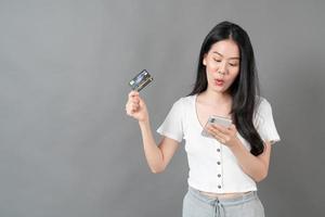 junge asiatische frau, die telefon mit hand hält, die kreditkarte hält - online-shopping-konzept foto
