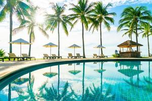 Wunderschöner Luxus-Sonnenschirm und -Stuhl um den Außenpool im Hotel und Resort mit Kokospalme am blauen Himmel