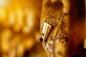 Nahansicht und Ernte ein Gold Blatt auf Hand von alt und golden Buddha Statue auf verschwommen golden Hintergrund foto