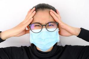 junge asiatische frau, die kopfschmerzen hat, während sie eine medizinische maske trägt, um schlechte luftverschmutzung zu schützen foto