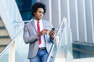 schwarzer Geschäftsmann mit einem Smartphone in der Nähe eines Bürogebäudes foto