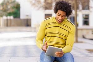 schwarzer Mann mit einem digitalen Tablet auf einer Bank im Freien sitzen. foto