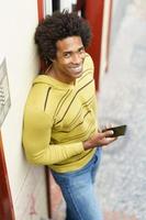 schwarzer Mann mit Afro-Haaren und Kopfhörern mit Smartphone.