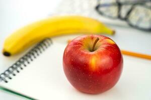 gesund Snack. ein rot Apfel auf ein leer Notizbuch auf das Tisch. zurück zu Schule. Nahansicht. selektiv Fokus. foto