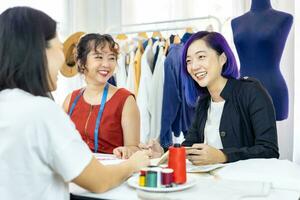 Mannschaft von modisch freiberuflich Schneiderinnen und Kunde wählen Design und Pantone zum Neu Benutzerdefiniert Kleid während Arbeiten im künstlerisch Werkstatt Studio zum Mode Design und Kleidung Geschäft Industrie foto