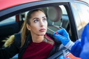 Porträt von Frau Fahrt durch Coronavirus covid-19 Prüfung durch medizinisch Mitarbeiter mit ppe passen durch Nase Tupfer. Neu normal Gesundheitswesen Fahrt durch Bedienung und medizinisch Konzept. foto