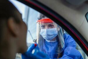 Arzt oder Krankenschwester tragen pp, n95 Maske, Gesicht Schild und persönlich schützend Kleid Stehen neben das Auto Straße Screening zum covid-19 Virus, Nasal- Tupfer prüfen. foto