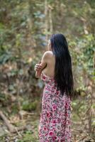 jung Frauen Tourist im Jahrgang Kleid steht allein auf Felsen durch Wasserfall im das Wald in der Hoffnung zu cool Nieder zum schwimmen. das zurück von jung asiatisch Frauen Tourist Wer genießt spielen im Wasserfall allein. foto