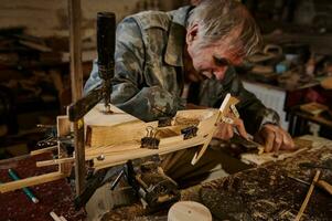 ein reifen Zimmermann funktioniert auf ein hölzern Spielzeug Segelboot im seine Werkstatt. Handwerker macht handgemacht hölzern Artikel foto